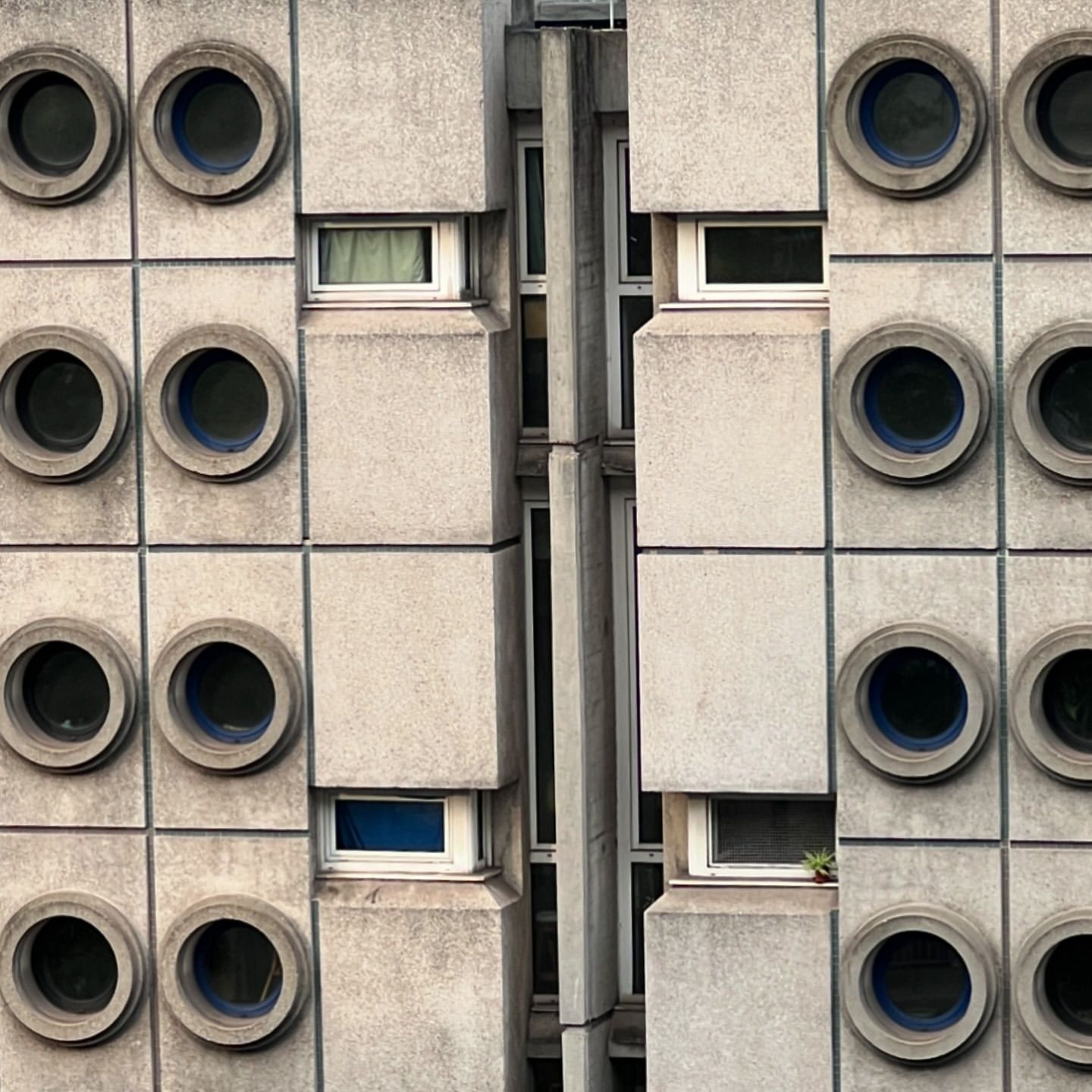 Exterior view of a high-rise building with concrete blocks, round windows, and some rectangular windows; architectural details in the city.