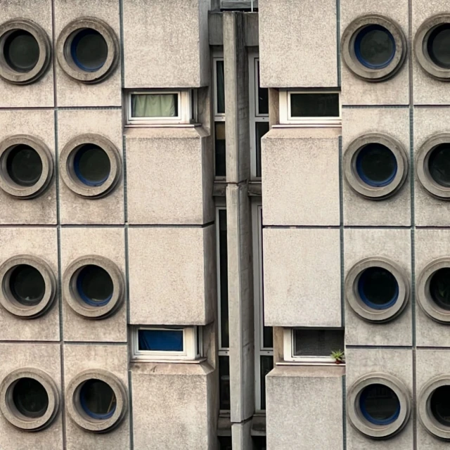 Exterior view of a high-rise building with concrete blocks, round windows, and some rectangular windows; architectural details in the city.