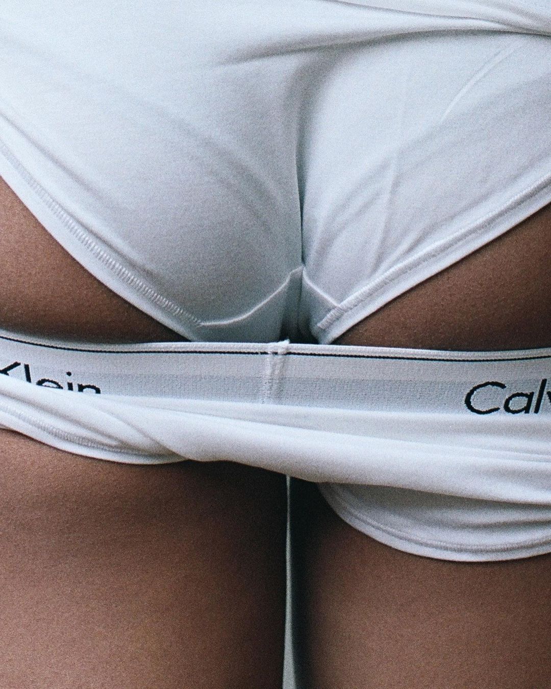 Close-up studio shot of a person wearing white Calvin Klein underwear and white top, showing the waist and upper thighs.