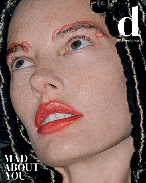 Close-up portrait of a female model with red lipstick and red eyebrow embellishments, looking up, with braided hair visible.