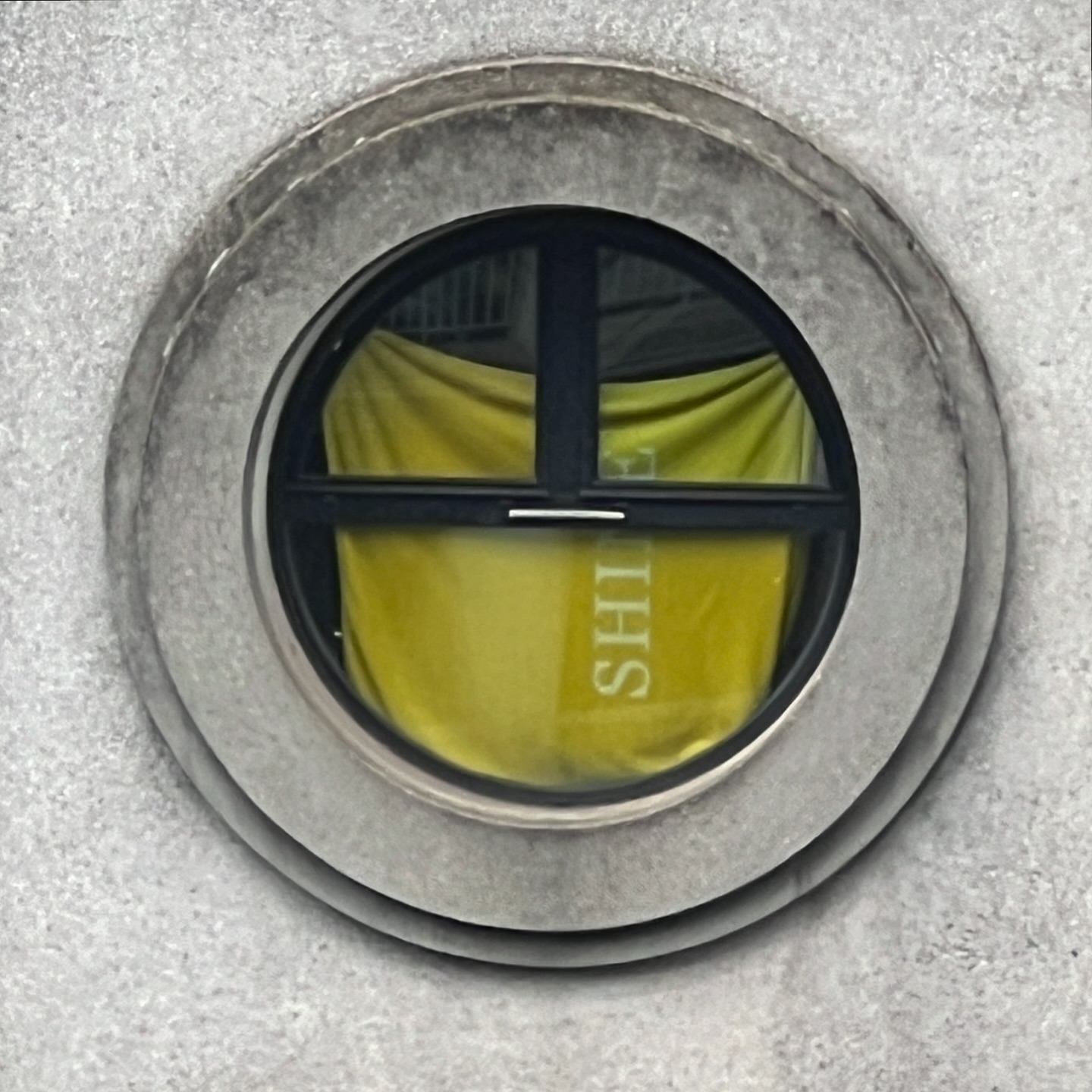 Exterior shot of a circular window in a stone wall, with a yellow cloth with white text inside the window, viewed up close.