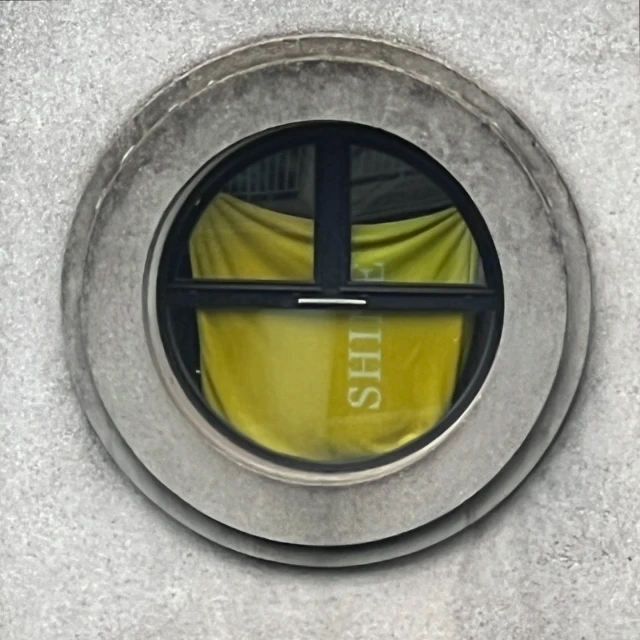 Exterior shot of a circular window in a stone wall, with a yellow cloth with white text inside the window, viewed up close.