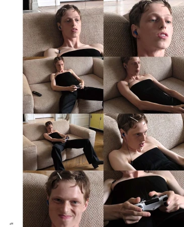A person with short brown hair, wearing a black strapless top and dark pants, sits on a couch and plays a video game with a white controller.