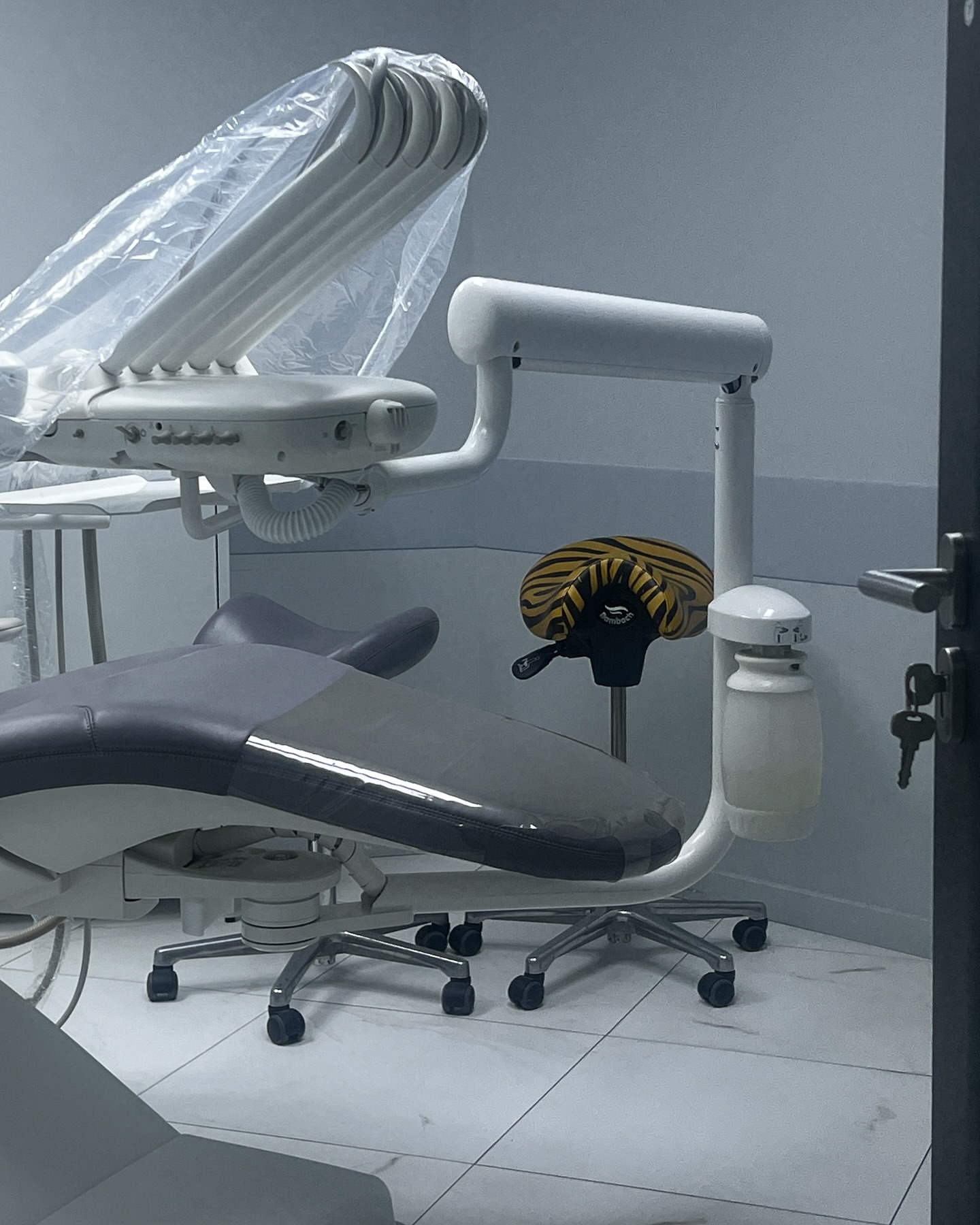 Dental examination room featuring an adjustable chair and overhead light with a white tiled floor in a healthcare setting.