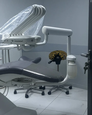 Dental examination room featuring an adjustable chair and overhead light with a white tiled floor in a healthcare setting.