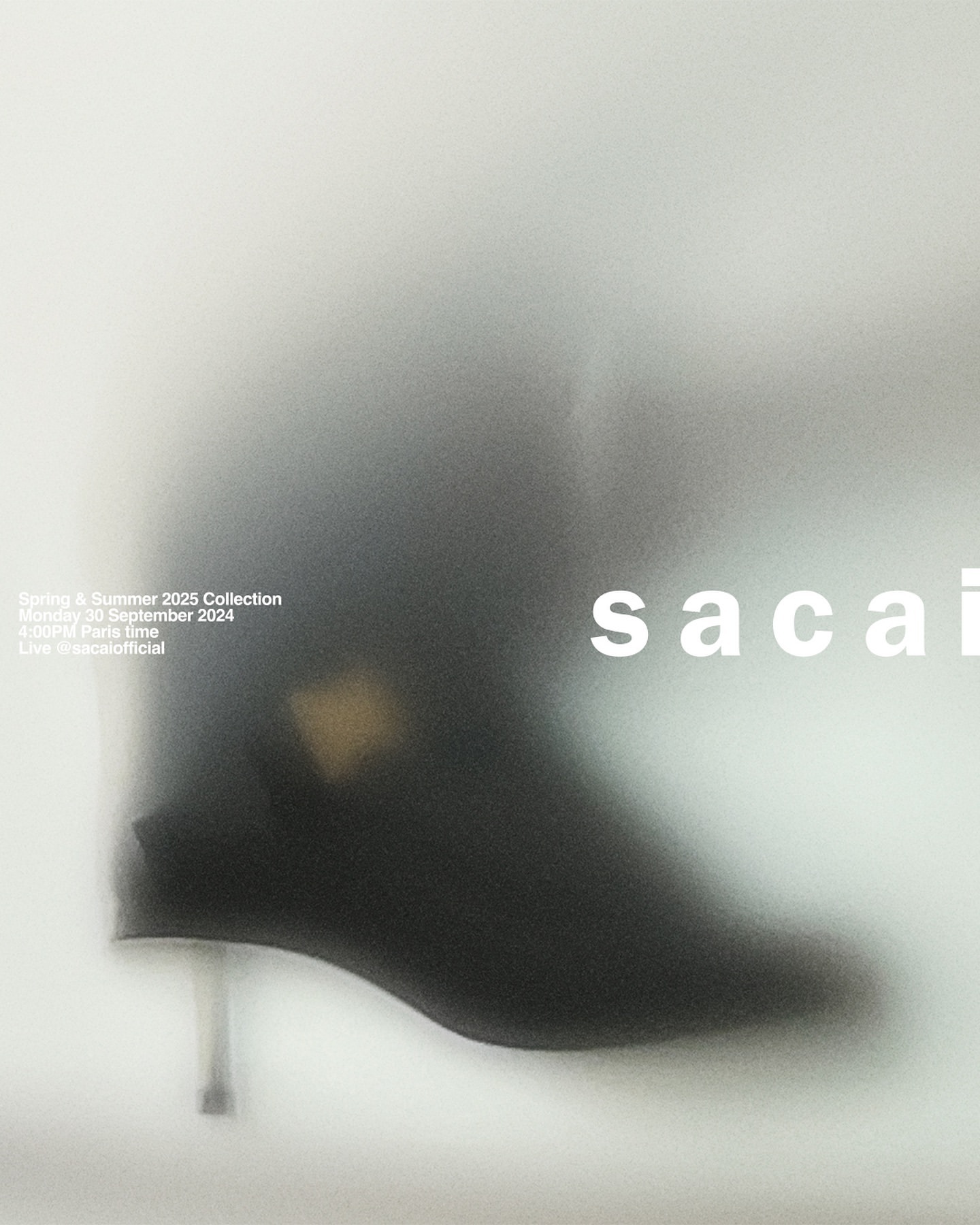 Fashion advertisement featuring a black ankle boot with a metallic heel, blurred against a light grey background with brand typography.