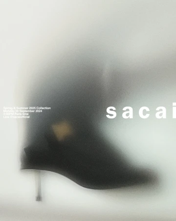 Fashion advertisement featuring a black ankle boot with a metallic heel, blurred against a light grey background with brand typography.