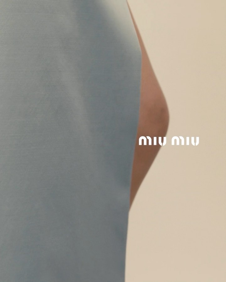 Close-up macro detail of blue fabric clothing surface with partial skin visible and white Miu Miu logo text