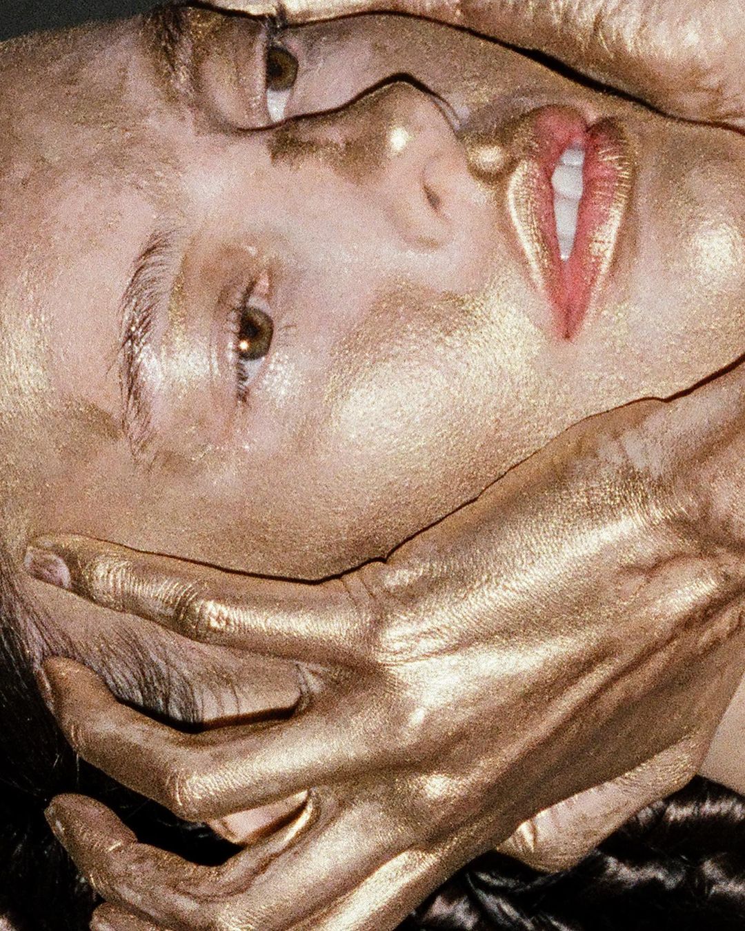 Surreal close-up of a woman with gold painted skin and hand covering her mouth, creating a striking beauty and fashion portrait.