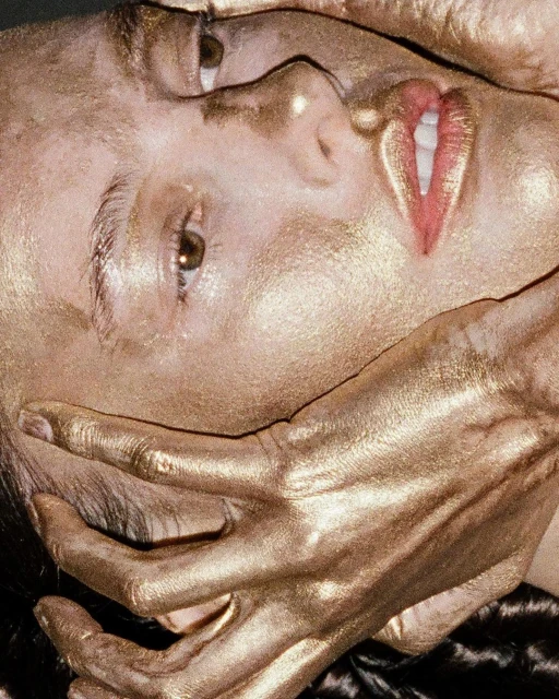 Surreal close-up of a woman with gold painted skin and hand covering her mouth, creating a striking beauty and fashion portrait.