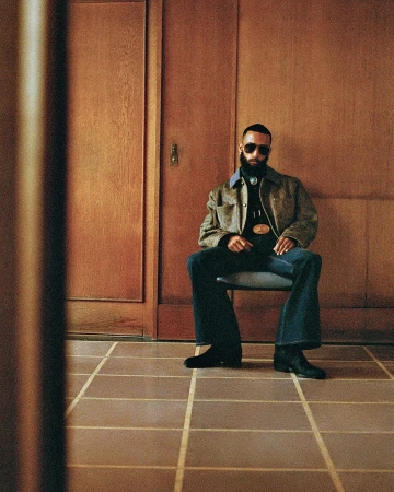 Man with beard and sunglasses seated on a chair in a wood-paneled room photographed by Tanya and Zhenya Posternak