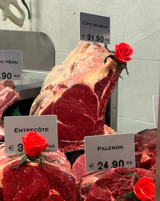Display of various raw meat cuts behind glass with price tags and decorative red roses, offering a butcher shop style presentation.