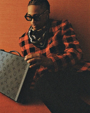 Young adult male with sunglasses poses indoors wearing a red plaid jacket, bandana, and holding a monogrammed Louis Vuitton case.