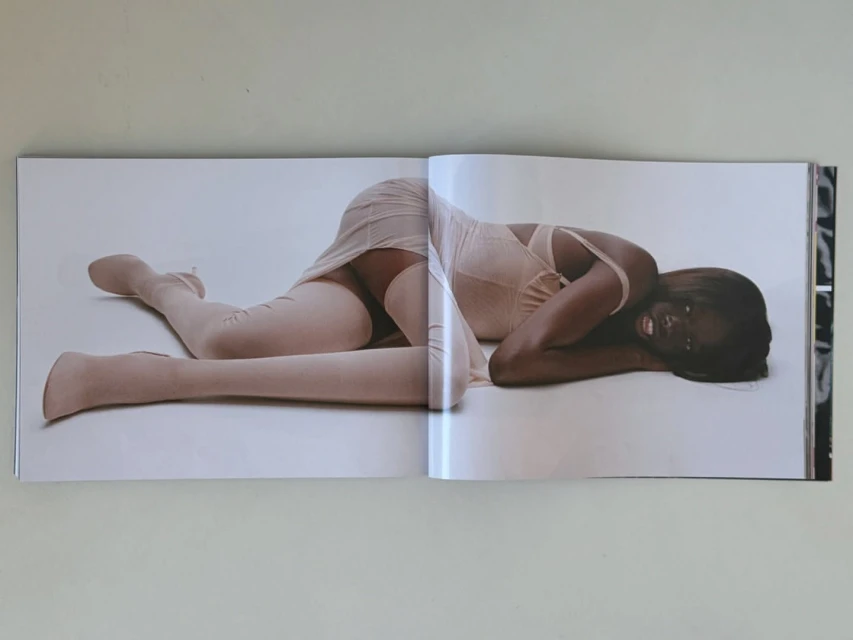 Photo of a Black female fashion model lying down in a photo studio wearing a pink corset-style dress and matching thigh-high stockings.
