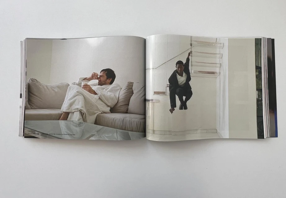 Magazine spread shows an adult male in robe with drink on couch, and a young person in a suit squatting on a stair landing.