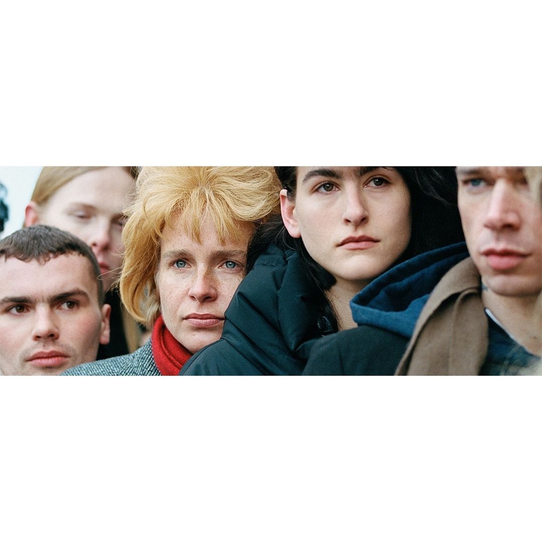 A group of five people with various expressions, standing close together, with a focus on their faces and upper torsos.