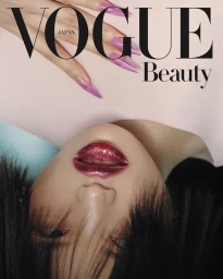Close-up portrait of a model with dark hair, glossy dark lips, and fingers with long purple translucent nails placed near the forehead.