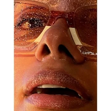Extreme close-up portrait of a person wearing tinted sunglasses covered in water droplets with wet skin