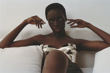 Black woman with short hair wearing a metallic silver bustier top posed against white pillows in London by Tanya and Zhenya Posternak