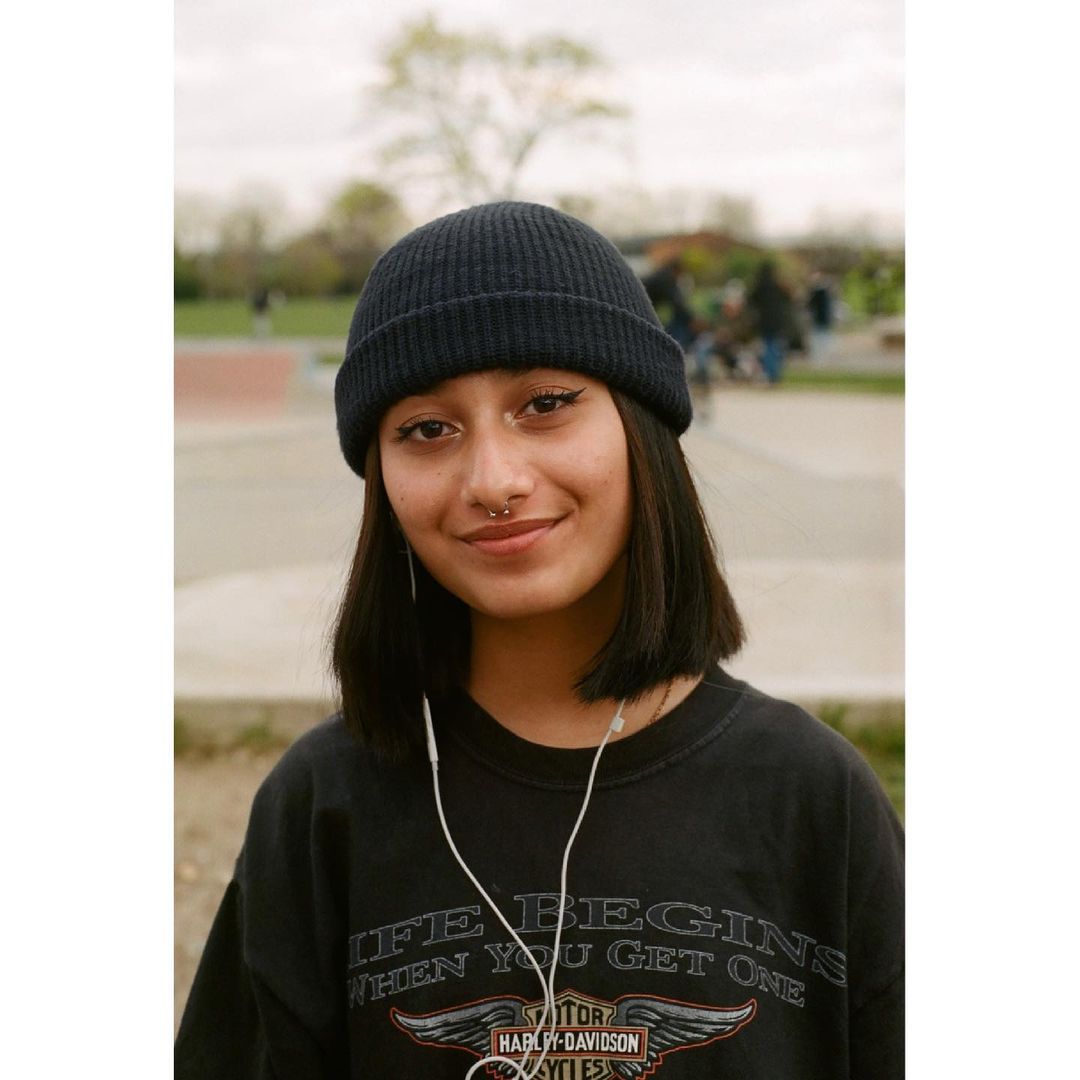 Portrait of a young woman in a beanie and vintage t-shirt smiling in an outdoor setting. Head and shoulders shot with soft natural light.