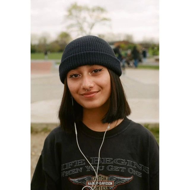 Portrait of a young woman in a beanie and vintage t-shirt smiling in an outdoor setting. Head and shoulders shot with soft natural light.