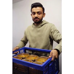 Man wearing a green hoodie holding a blue plastic crate filled with packaged food containers