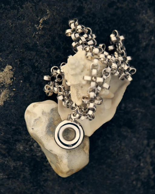 Silver chain necklace with round pendant on top of white stones and dark textured background, product photography, close-up.