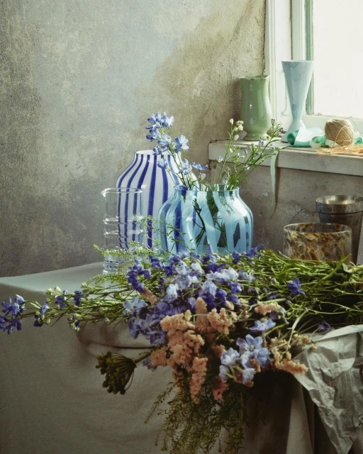 Striking still life photo showcases an assortment of vases with blue stripes filled with flowers on a table, near a window, indoor.