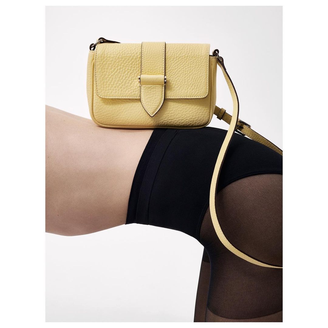 Yellow leather purse on person's leg with black tights. Simple product shot. Fashion, handbag, legwear, studio shot, white background.