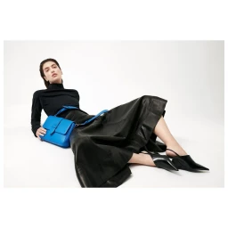 Woman in black top and long leather skirt reclining with a bright blue shoulder bag on white background
