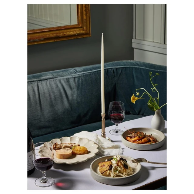 Elegant dining scene showcases plated appetizers, red wine, a slender candle, and a yellow flower arrangement in a dimly lit setting.
