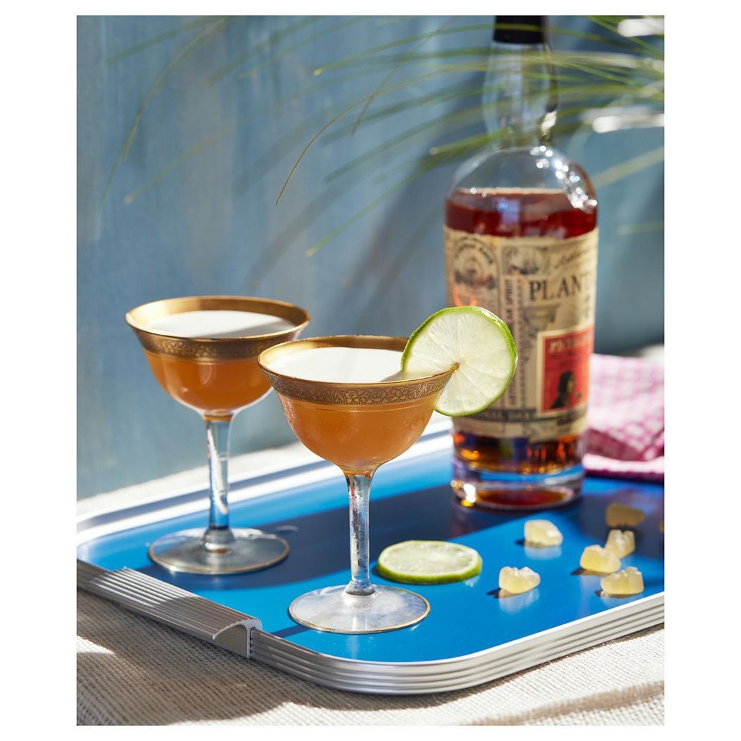 Two stemmed glasses of cocktails next to a rum bottle, garnished with lime slices on a blue tray, creating an inviting drink setup.