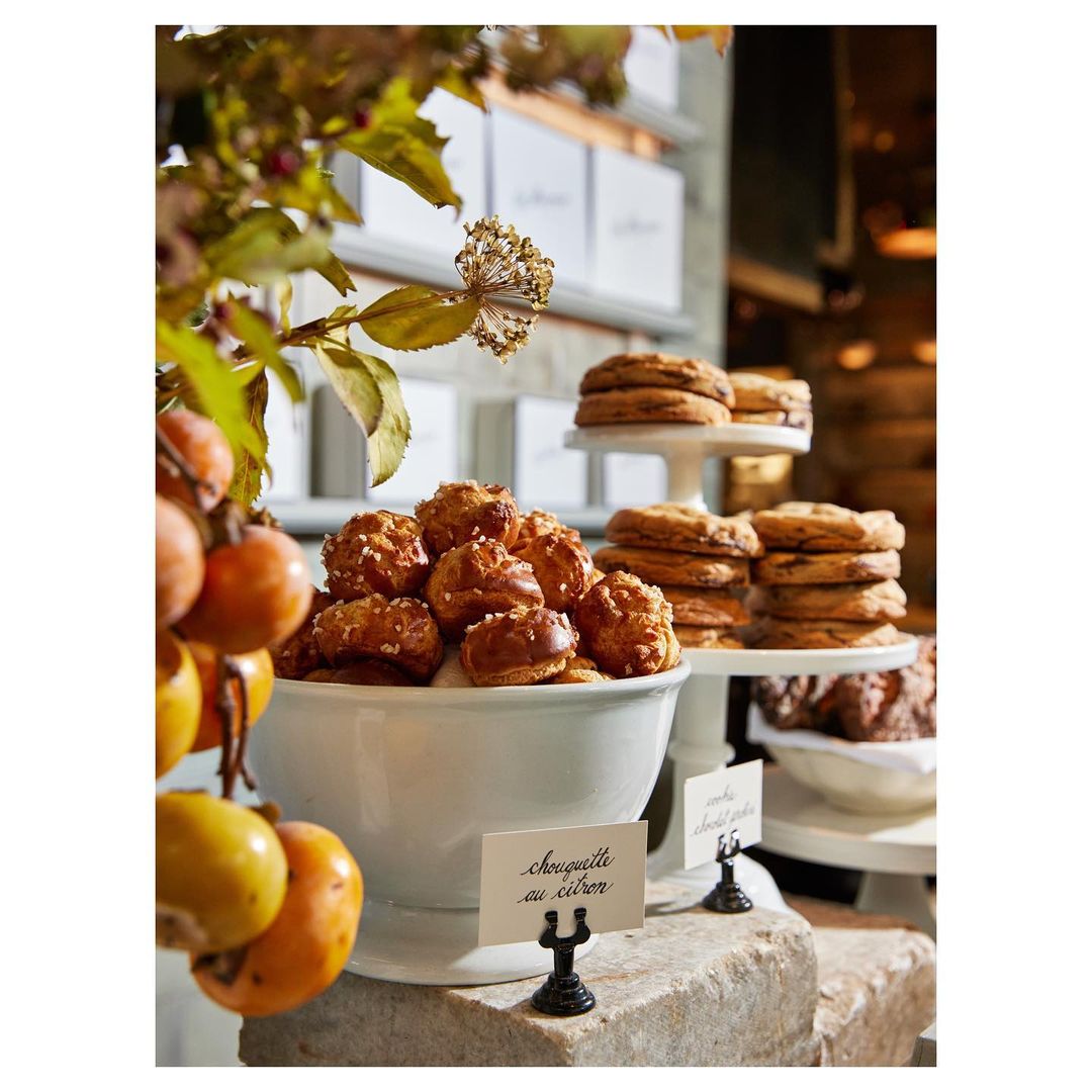 A display of pastries in a bakery featuring chouquettes au citron and cookies on tiered stands, complemented by floral decorations.
