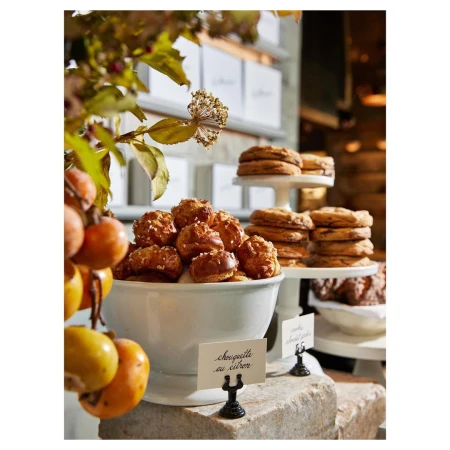 A display of pastries in a bakery featuring chouquettes au citron and cookies on tiered stands, complemented by floral decorations.