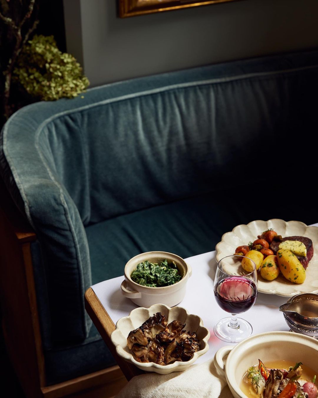 Overhead shot of an elegant dining table featuring an assortment of dishes, including meat, potatoes, vegetables, and a glass of red wine.