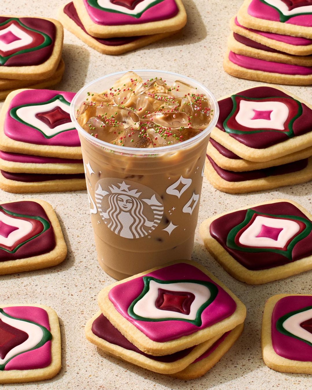 Iced coffee beverage from Starbucks in a plastic cup surrounded by stacks of square sugar cookies decorated with pink, white, and maroon icing.
