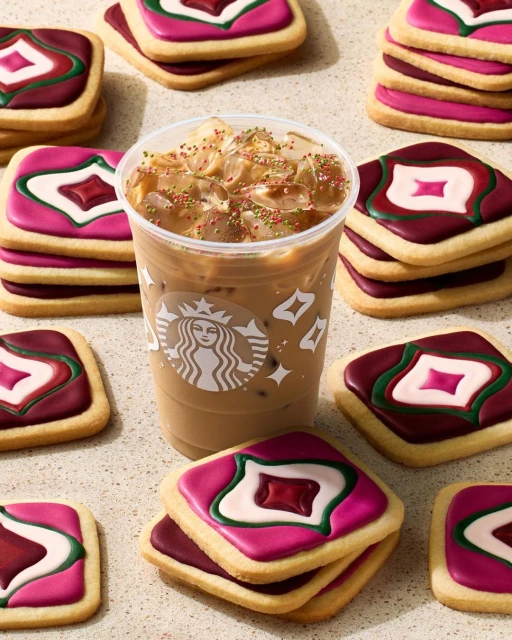 Iced coffee beverage from Starbucks in a plastic cup surrounded by stacks of square sugar cookies decorated with pink, white, and maroon icing.