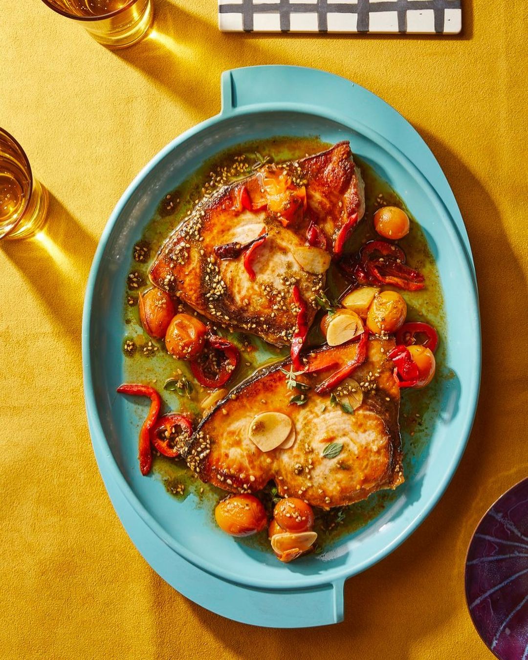 Overhead shot of a dish featuring two slices of cooked fish garnished with tomatoes, peppers and garlic, set on a bright blue serving platter.