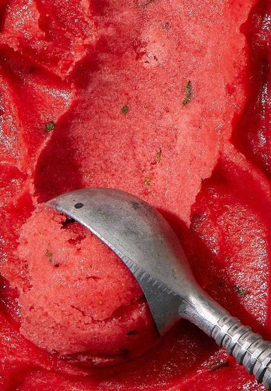 Close-up of refreshing watermelon sorbet with spearmint, scooped with a silver spoon. Brightly lit with vibrant reds and greens.