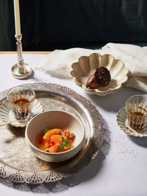 Elevated shot of a citrus fruit salad and espresso on a decorative silver tray, complemented by a candle and dark backdrop.