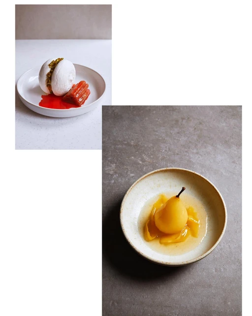 Overhead shot of two plates featuring poached pear and meringue-based desserts drizzled with fruit sauce, set against light grey backgrounds.