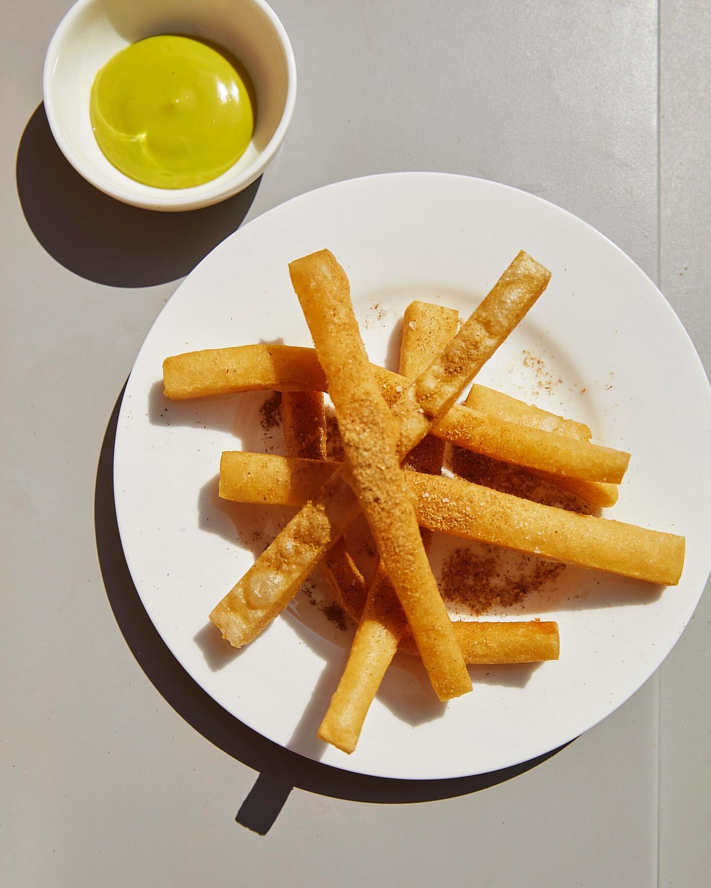 Overhead shot of crispy yucca fries on a white plate, served with a vibrant green dipping sauce in a matching white bowl.
