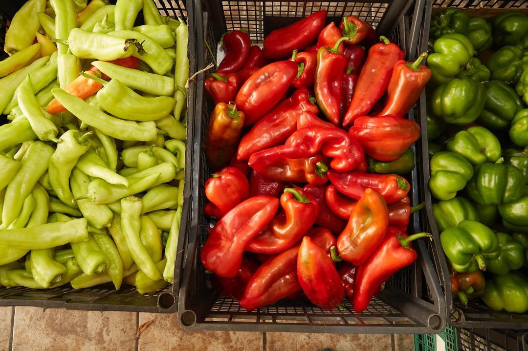 Overhead shot of three crates filled with vibrant green, red, and yellow peppers, showcasing the fresh produce's colors and textures.