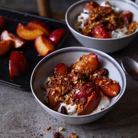 Close-up of two bowls filled with plums, granola, and yogurt, showcasing a delicious and healthy dessert or breakfast option.