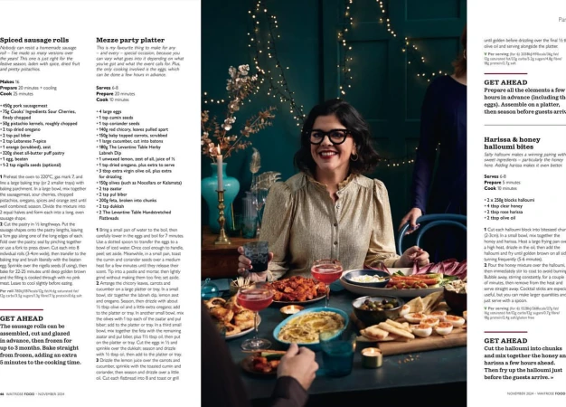 Smiling woman in glasses seated at table with food, drinks, and festive lights in a warm, inviting indoor setting; holiday party.