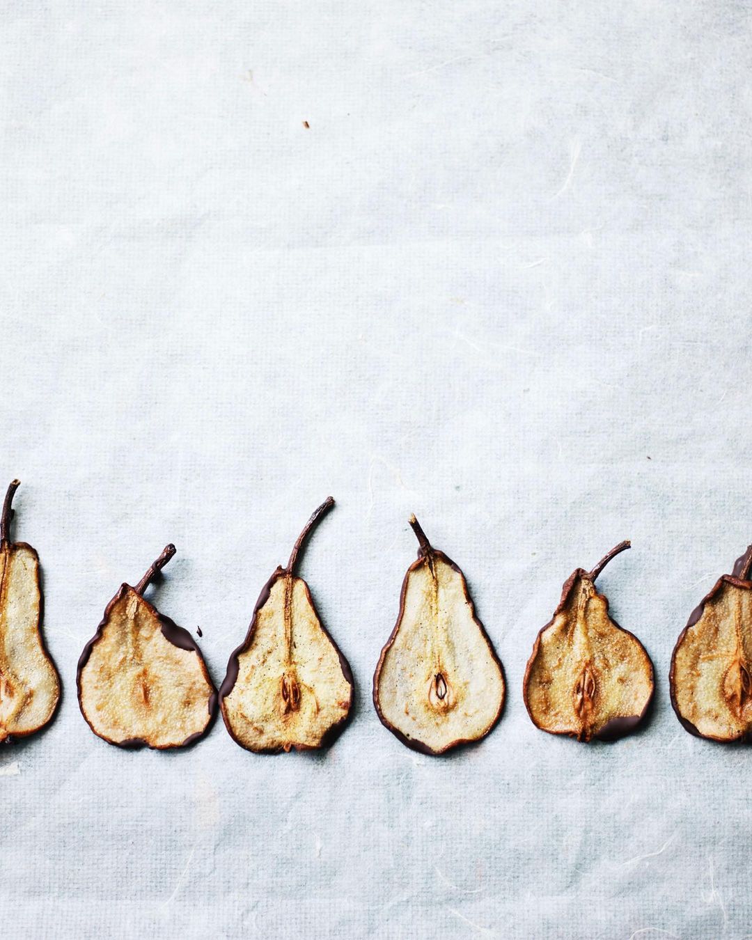 Overhead shot of a row of dried pear slices dipped in chocolate on white parchment paper. Food photography, fruit snack.