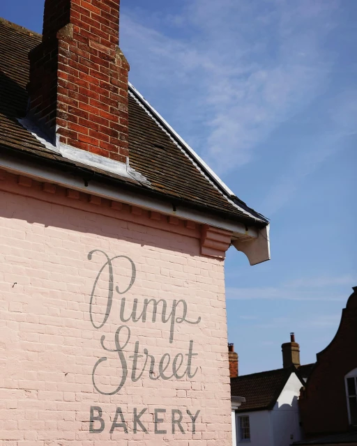 Charming bakery exterior with weathered pink brick, brick chimney, and vintage signage on a sunny day with a blue sky backdrop.