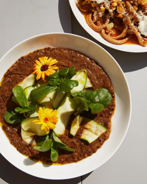Overhead shot of two plates with pasta. One plate has spiral pasta with sauce, zucchini and flowers. The other has a tomato sauce.