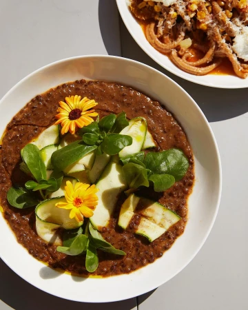Overhead shot of two plates with pasta. One plate has spiral pasta with sauce, zucchini and flowers. The other has a tomato sauce.