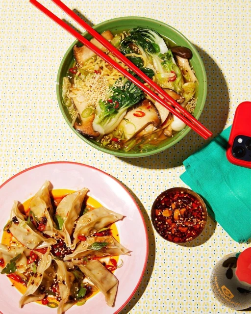 Overhead shot of dumpling and ramen dishes featuring bold colors and a bright, patterned background, capturing an inviting, close-up food layout.